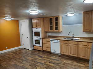 Kitchen featuring white appliances, a sink, a textured ceiling, glass insert cabinets