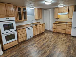 Kitchen with a sink, white appliances, under cabinet range hood, light brown cabinetry