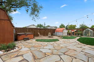 View of flagstone patio with a fenced backyard, a hot tub, an outbuilding, a greenhouse, and a storage shed