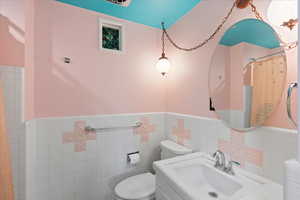 Hall full bathroom featuring a sink, toilet, and tile walls