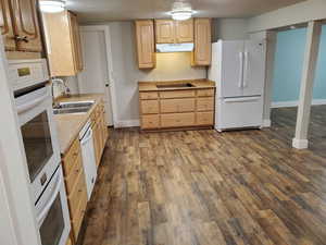 Kitchen with white appliances, a sink, under cabinet range hood, light brown cabinetry