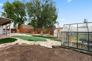 Fenced backyard featuring an outbuilding, a greenhouse, a patio, a hot tub, and a storage unit