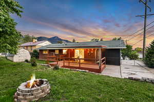 Back of house at dusk featuring a fire pit, a storage unit, a patio, an outdoor structure, and a wooden deck