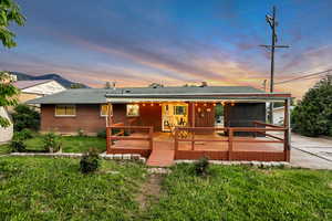 View of front of property featuring brick siding, a wooden deck, roof with shingles, and a front lawn