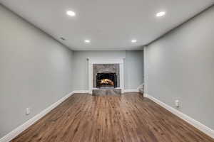 Unfurnished living room with a tiled fireplace, recessed lighting, baseboards, dark wood-style floors, and stairs