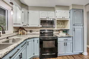 Kitchen featuring stainless steel microwave, black / electric stove, a sink, and decorative backsplash