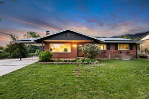 View of front of property with brick siding, roof mounted solar panels, concrete driveway, a front lawn, and a chimney