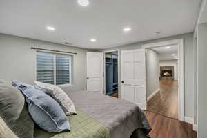 Bedroom featuring wood finished floors, recessed lighting, baseboards, a fireplace, and a walk in closet