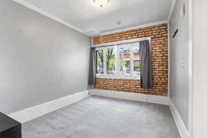 Carpeted spare room featuring a textured ceiling, crown molding, brick wall, and baseboards
