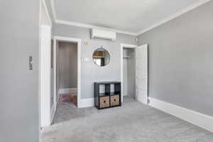 Unfurnished bedroom with a wall mounted air conditioner, carpet flooring, a textured ceiling, ornamental molding, and baseboards