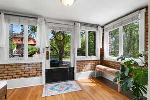 Sunroom featuring healthy amount of natural light, wood finished floors, brick wall, and baseboards