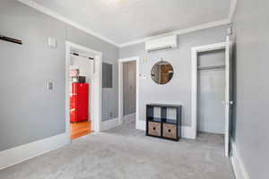 Unfurnished bedroom with a wall mounted air conditioner, carpet flooring, crown molding, electric panel, and a closet