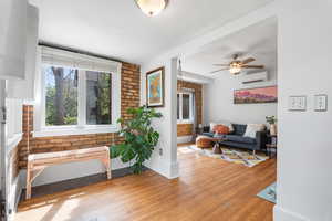 Living room with a wall unit AC, wood finished floors, ceiling fan, brick wall, and a textured ceiling