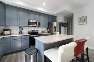 Kitchen with stainless steel appliances, dark wood-type flooring, a kitchen breakfast bar, backsplash, and light countertops