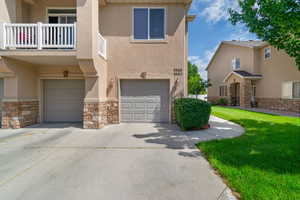 View of front of home featuring stone siding, an attached garage, stucco siding, driveway, and a balcony