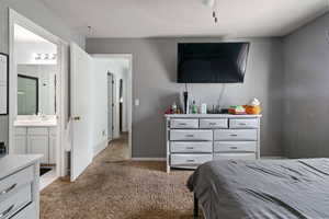 Carpeted bedroom featuring a sink, connected bathroom, and baseboards