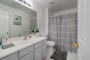 Bathroom with marble look tile flooring, vanity, toilet, a textured ceiling, and curtained shower