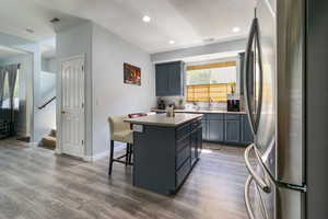 Kitchen with freestanding refrigerator, a kitchen island, a breakfast bar area, dark wood-type flooring, and decorative backsplash