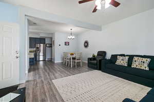 Living area featuring dark wood-style floors, ceiling fan, baseboards, and a chandelier