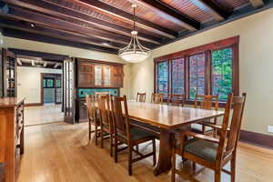 Dining area with beamed ceiling, light wood-type flooring, wooden ceiling, baseboards, and a chandelier