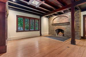 Unfurnished living room with beamed ceiling, wood-type flooring, a fireplace, and baseboards