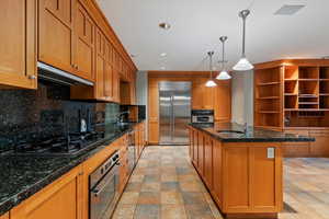 Kitchen with appliances with stainless steel finishes, ventilation hood, a sink, brown cabinets, and recessed lighting