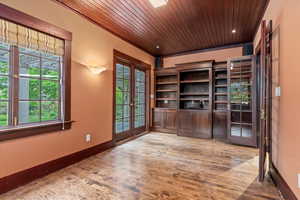 Unfurnished office featuring french doors, wood ceiling, plenty of natural light, wood finished floors, and baseboards
