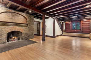 Unfurnished living room with hardwood / wood-style floors, beam ceiling, stairs, baseboards, and a brick fireplace