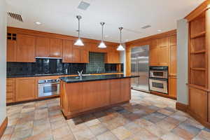 Kitchen featuring stainless steel appliances, a center island with sink, backsplash, a sink, and recessed lighting