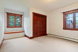 Unfurnished bedroom with multiple windows, wallpapered walls, a baseboard heating unit, carpet, and a closet
