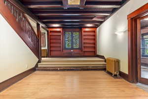 Staircase with radiator heating unit, wood-type flooring, beam ceiling, and plenty of natural light