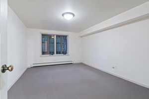 Empty room with a baseboard heating unit, carpet, and baseboards