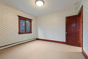 Carpeted spare room featuring a baseboard heating unit, a smoke detector, and wallpapered walls