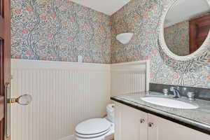 Bathroom with wallpapered walls, toilet, and vanity