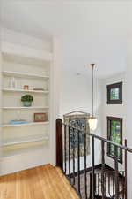Hall with an upstairs landing, built in shelves, and wood finished floors