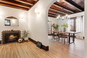 Sitting room featuring beam ceiling, wood finished floors, a chandelier, arched walkways, and a warm lit fireplace