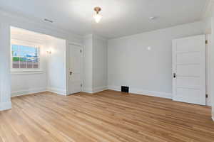 Empty room featuring baseboards, light wood finished floors, crown molding, and a smoke detector