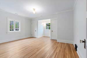 Unfurnished bedroom featuring multiple windows, light wood-type flooring, crown molding, and baseboards