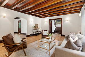 Living room with arched walkways, stairway, beam ceiling, wood finished floors, and baseboards