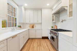 Kitchen featuring stainless steel range, a sink, backsplash, custom range hood, and white cabinets