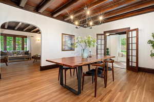 Dining room featuring french doors, beam ceiling, light wood-style flooring, baseboards, and arched walkways