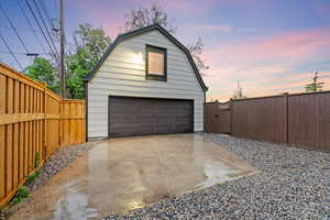 Garage at dusk featuring a detached garage, fence, and a gate