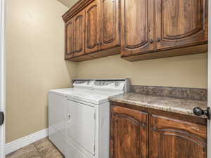 Clothes washing area with washing machine and dryer, cabinet space, and baseboards