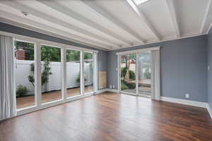 Unfurnished room featuring healthy amount of natural light, baseboards, beamed ceiling, and wood finished floors