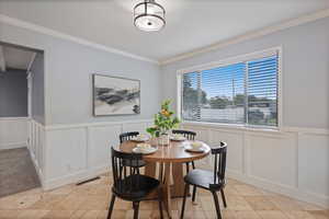 Dining space with ornamental molding, a wainscoted wall, a decorative wall, and light tile patterned floors
