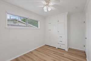 Unfurnished bedroom with light wood-type flooring, crown molding, baseboards, a closet, and a ceiling fan