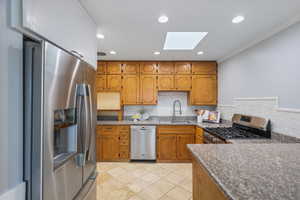 Kitchen featuring appliances with stainless steel finishes, a sink, a skylight, brown cabinets, and backsplash