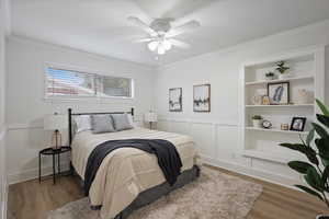 Bedroom featuring crown molding, wood finished floors, ceiling fan, and a wainscoted wall