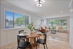 Dining room with ornamental molding, a wainscoted wall, a decorative wall, and light tile patterned floors