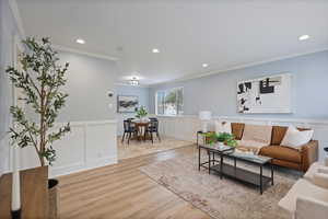 Living area with crown molding, wood finished floors, a decorative wall, recessed lighting, and wainscoting